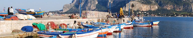 small colorful fisher boats docked in Mondello with Monte Pellegrino in the background, azure sky deep blue sea