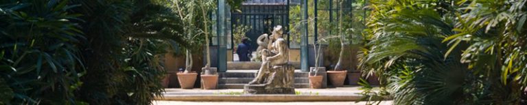 The central greenhouse of the botanic garden of Palermo with a classic statue at the entrance, lush growing plant everywhere